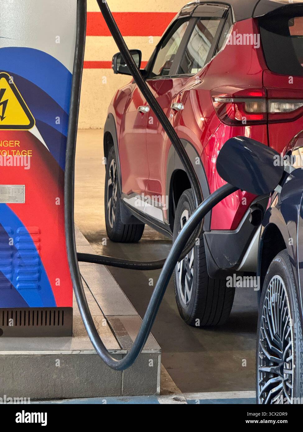 An electric vehicle on charge with a petrol vehicle parked opposite it in a shopping centre - Smartphone Captured Stock Image