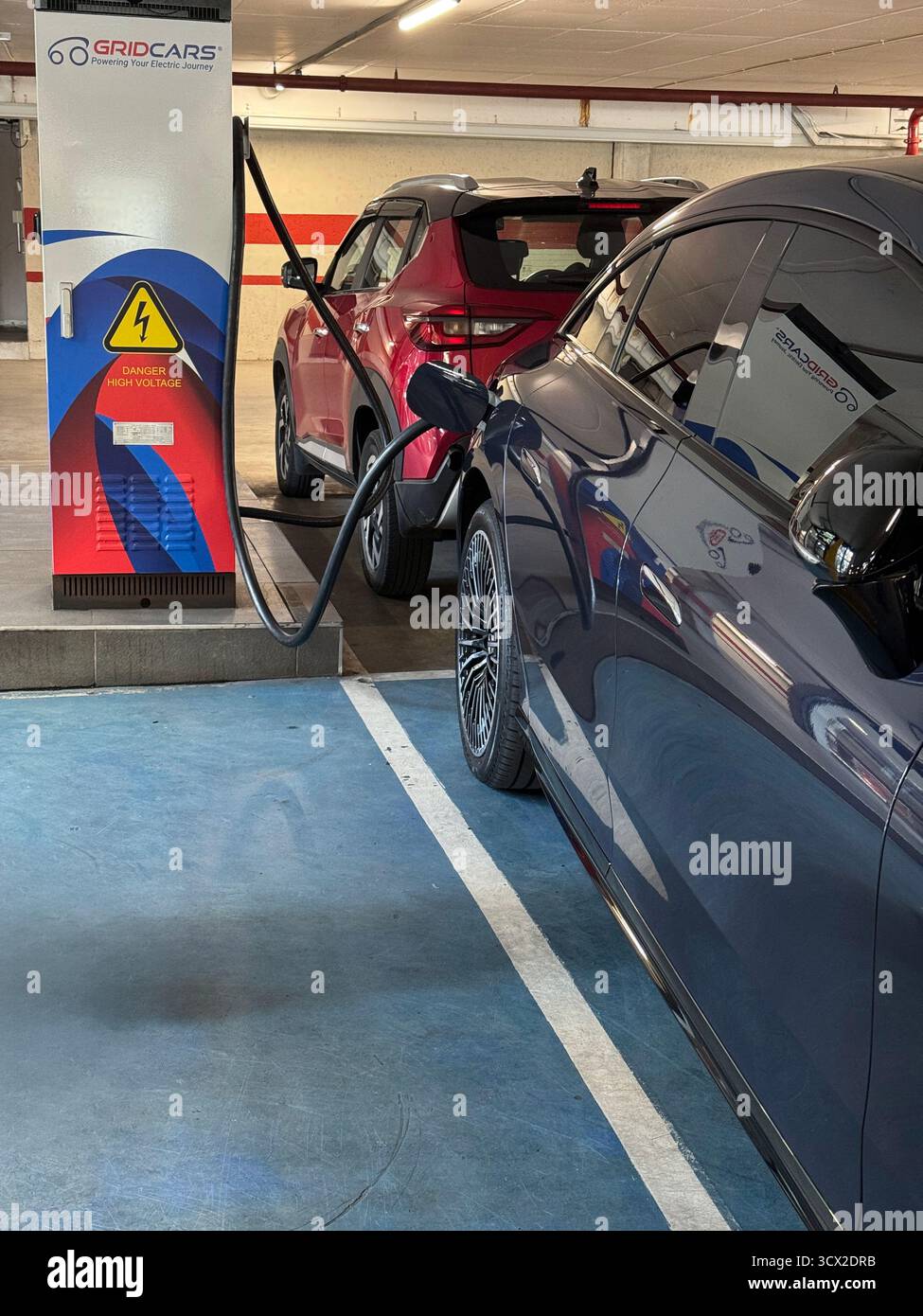 An electric vehicle on charge with a petrol vehicle parked opposite it in a shopping centre - Smartphone Captured Stock Image