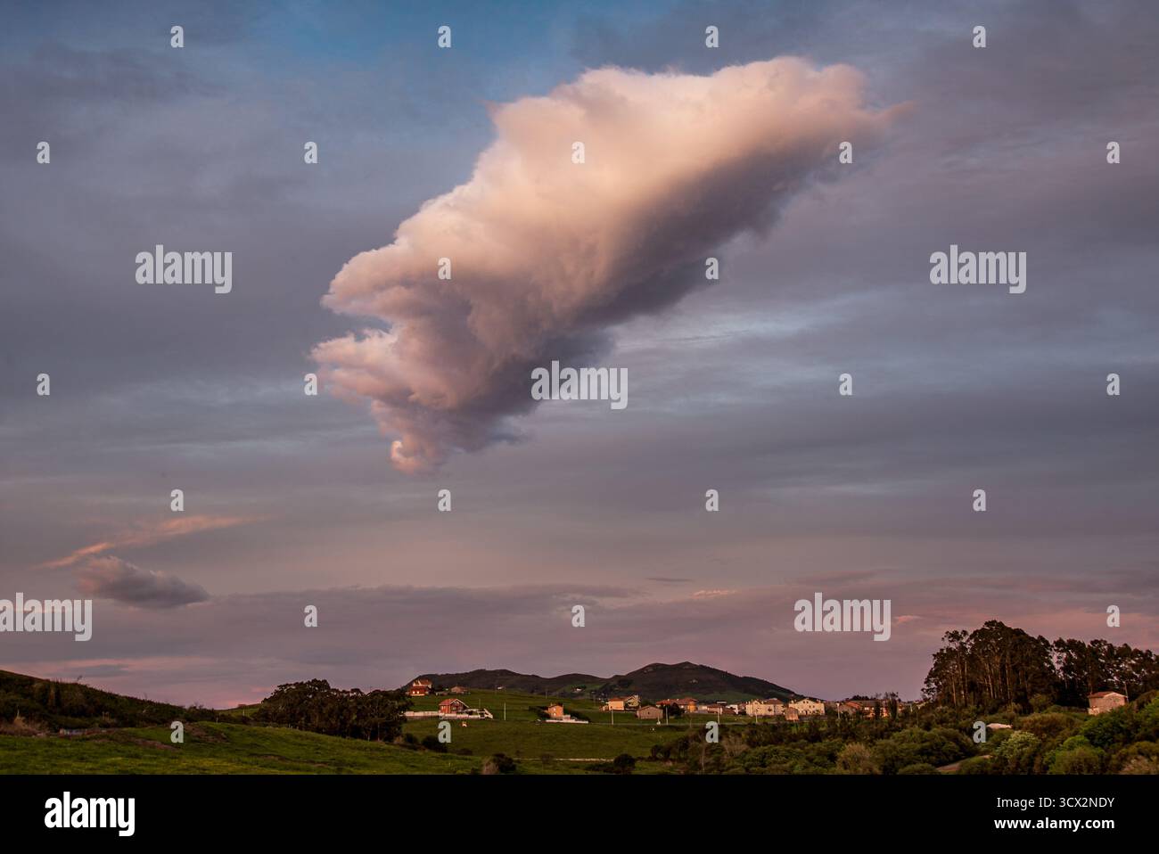 Dramatic isolated cloud over the rural hills and village of Miengo, Cantabria, northern Spain, at dusk Stock Photo