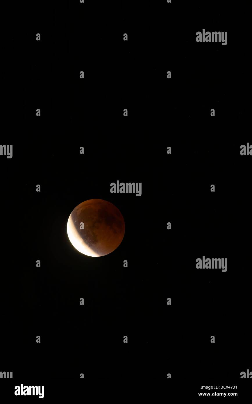 Moon passing through a partial lunar eclipse, casting an orange red shadow Stock Photo