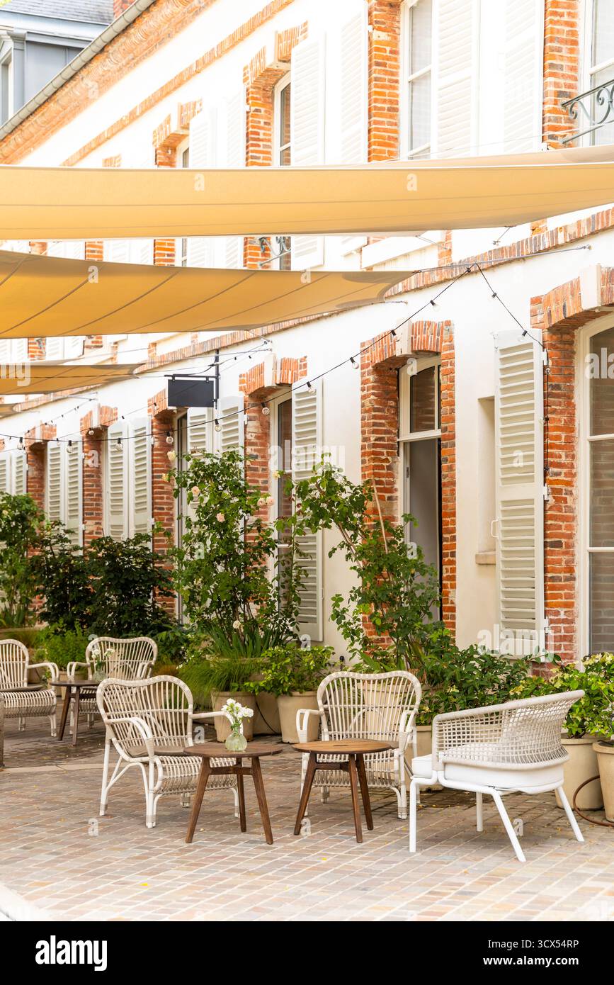 Inviting outdoor patio seating with chairs and tables under shade sails in a charming courtyard Stock Photo