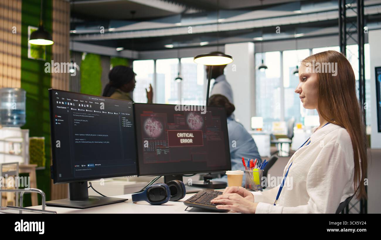 Young inexperienced developer in office struggling to fix critical error warning popup. Intern troubleshooting error notification on computer screen interrupting workflow, camera A Stock Photo