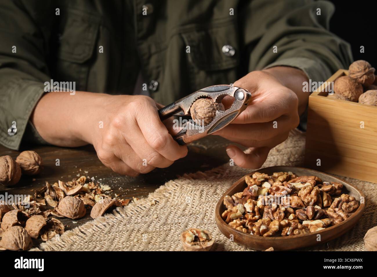Woman cracking walnuts with nutcracker on wooden table Stock Photo