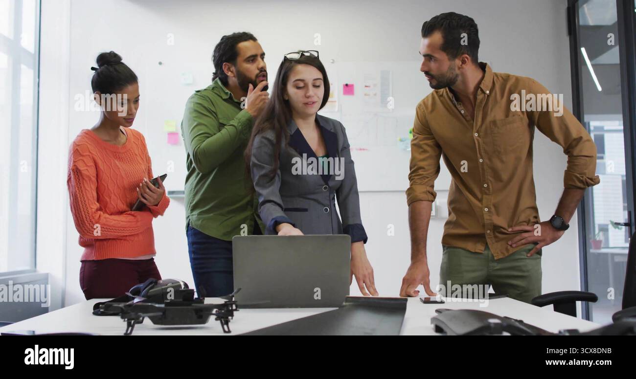 Gesturing lead in grey blazer directing discussion at meeting room, with laptop and drone prototype Stock Photo