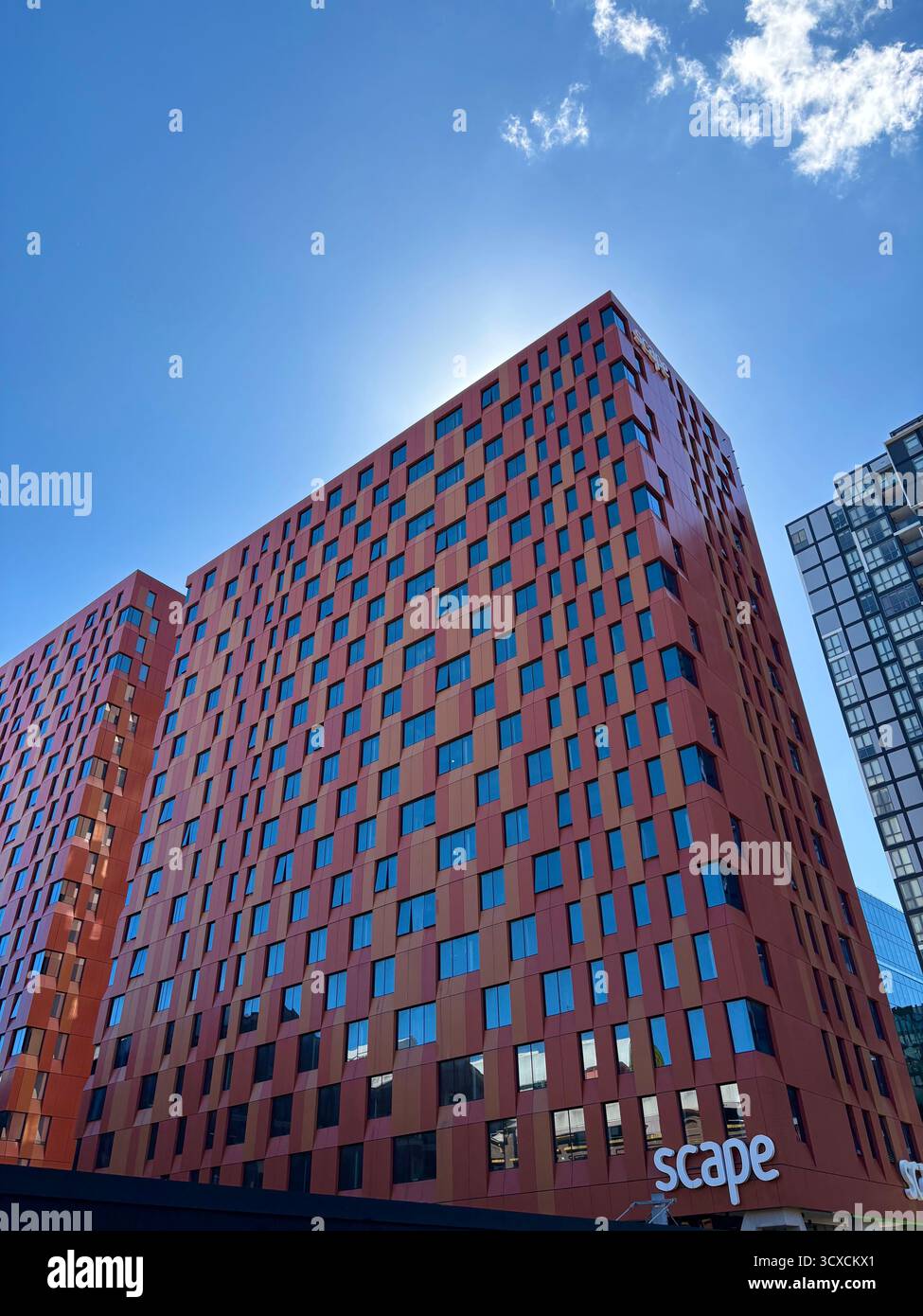 A bold red Scape building rises under a clear blue sky, its modern design and striking windows making it a standout in the urban skyline. - Smartphone Captured Stock Image