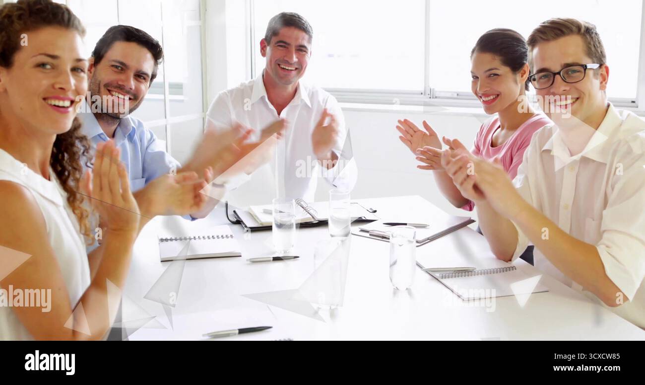 Applauding group of six professionals seated around conference table in office with notebooks, pens Stock Photo