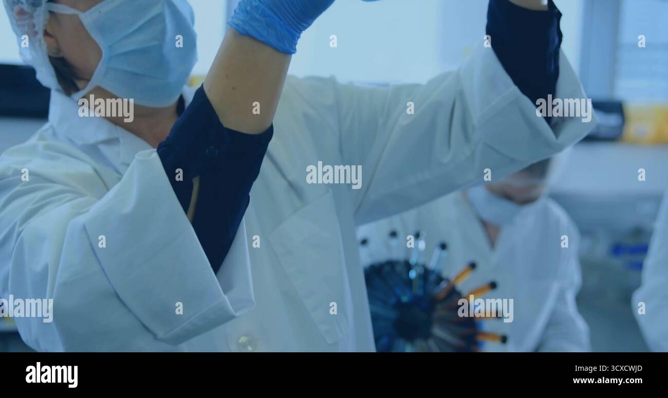 Inspecting lab-coated gloved technician raising vial toward light at ...