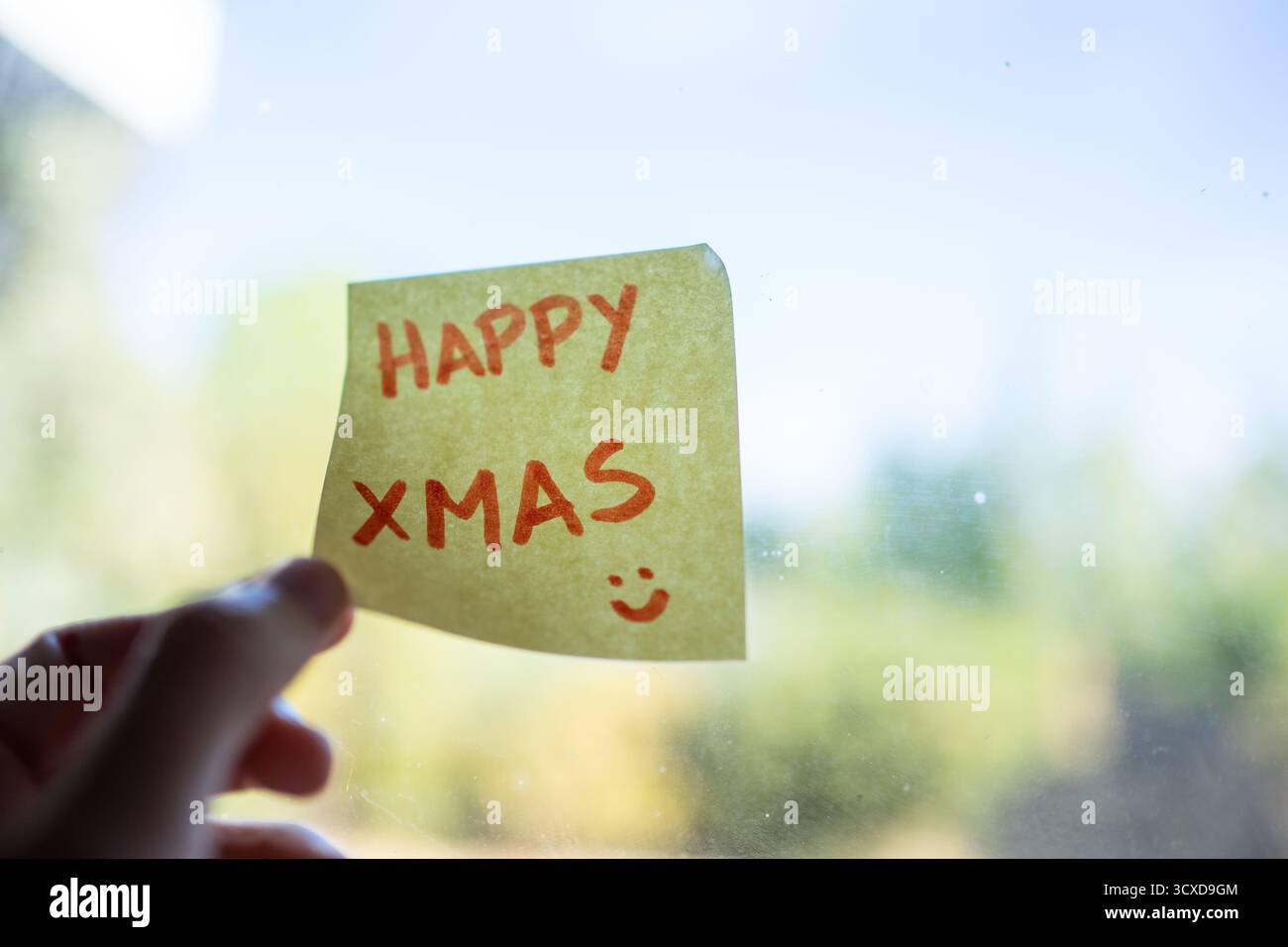 Hand posting a handwritten happy xmas greeting on a window with a smiley face Stock Photo