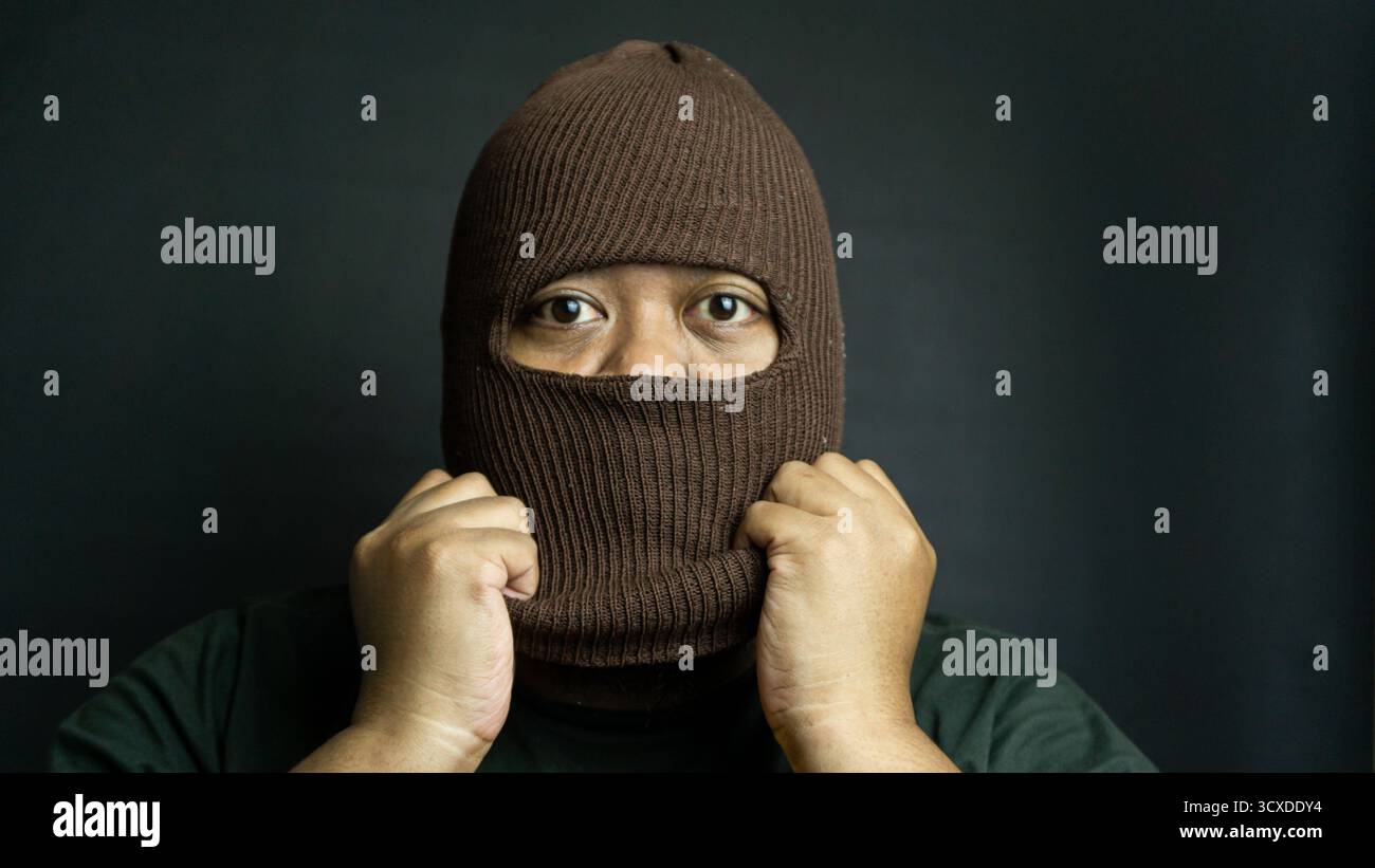 Man wearing brown cloth eye mask on black background, mysterious hidden identity with visible eye area and dramatic low-key portrait lighting Stock Photo