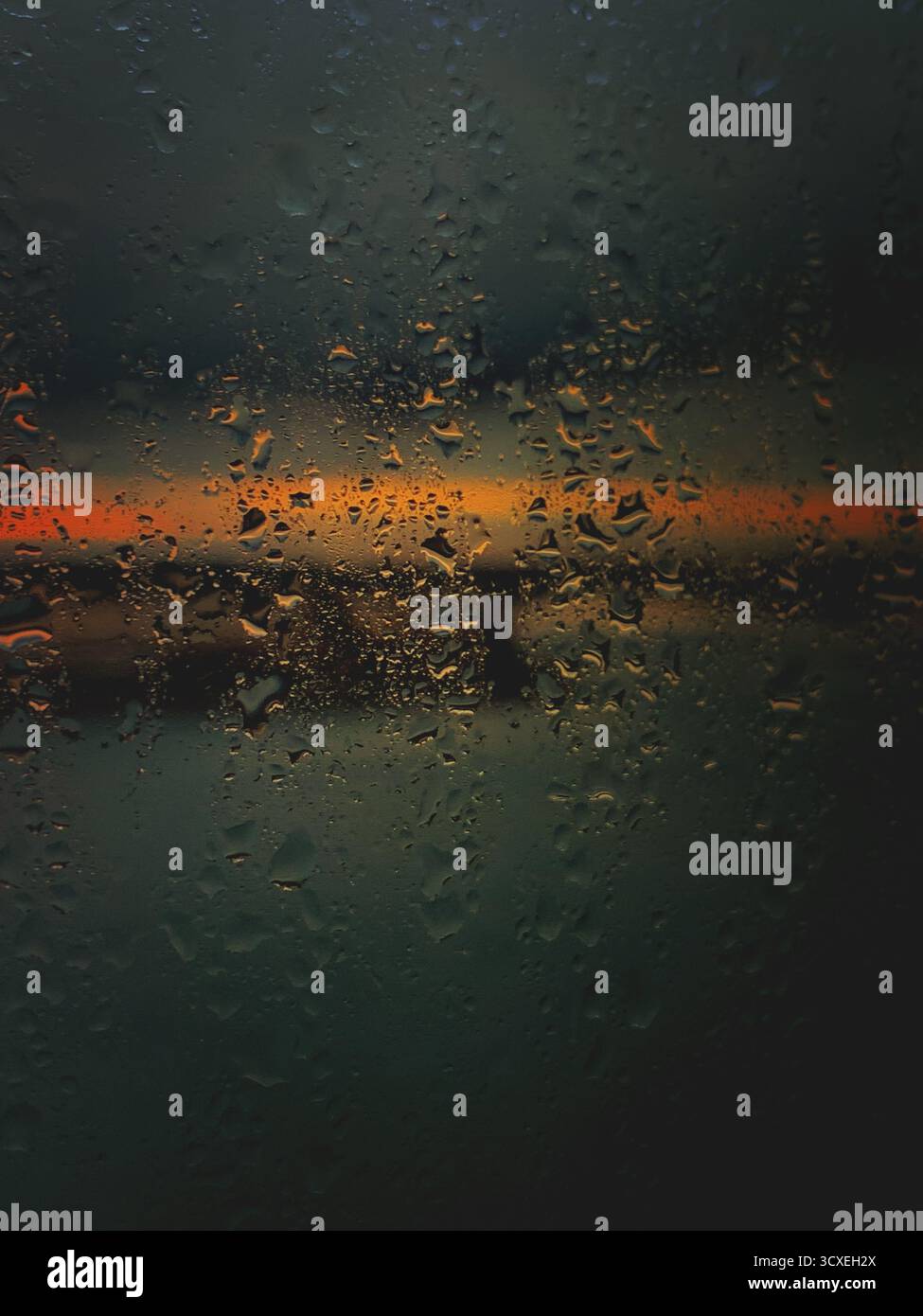 A wet window with water droplets and an orange sunrise strip of light with dark clouds window background Stock Photo