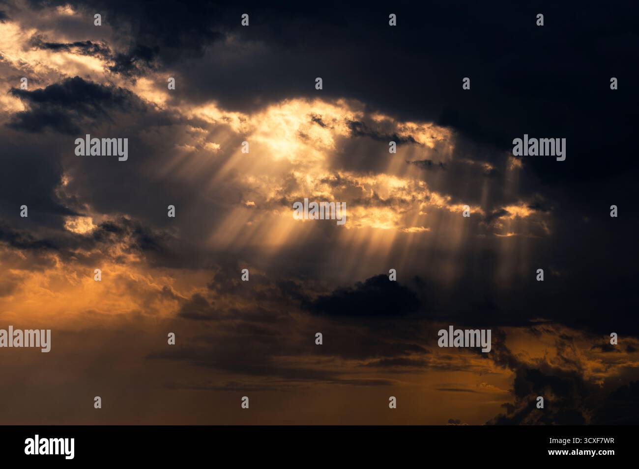 Sun rays shining through dramatic clouds at sunset Stock Photo