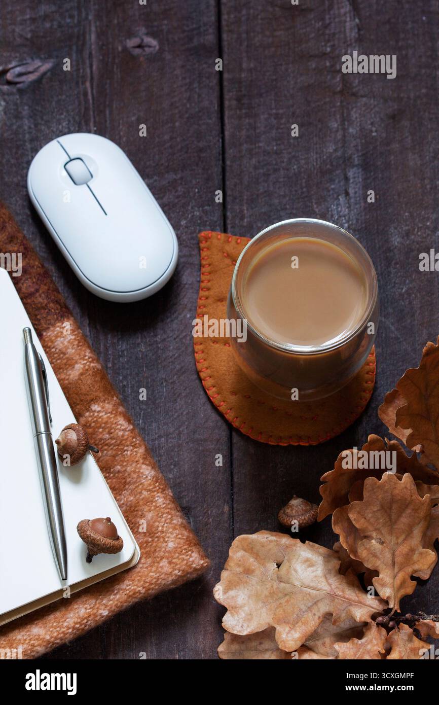 Business concept. A cozy autumn still life with office supplies, a computer mouse, pen, notebook, coffee, and a scarf. Rustic style. Stock Photo
