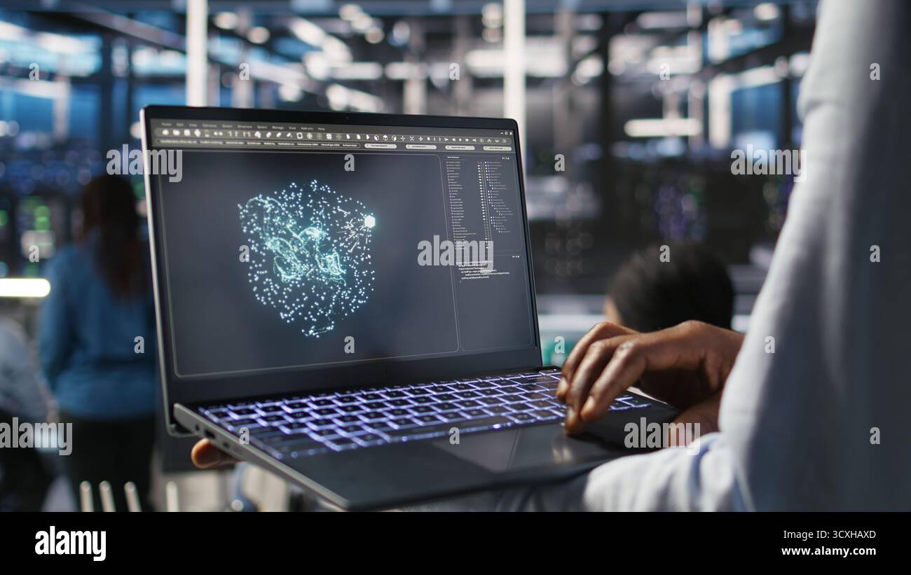 Close up of data center worker using laptop to interpret AI generated data analytics graphs. Server room technician using artificial intelligence on notebook displaying system metrics, camera A Stock Photo