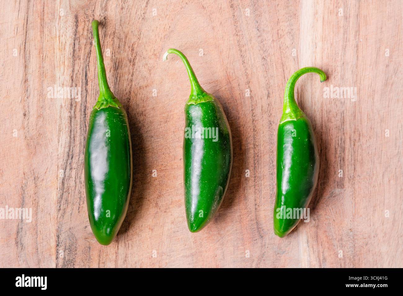 Three whole jalapeno peppers lined up on a wood cutting board Stock Photo