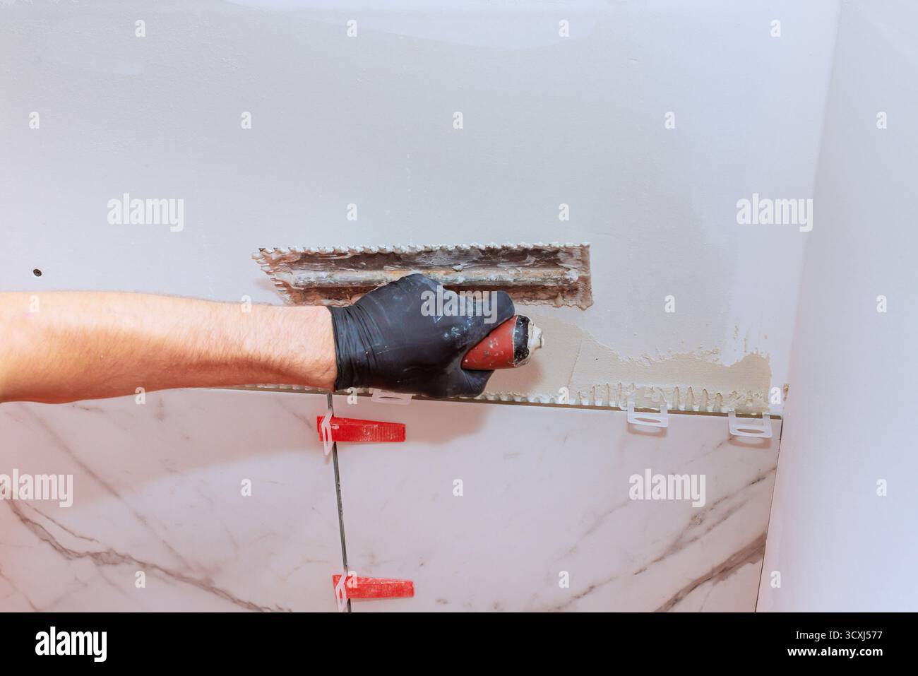 Construction worker uses trowel to spread tile adhesive on wall during bathroom remodel Stock Photo