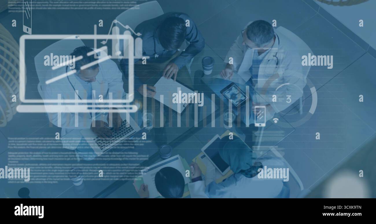 Collaborating team leaning over charts around glass table in office, with laptops and stethoscopes Stock Photo