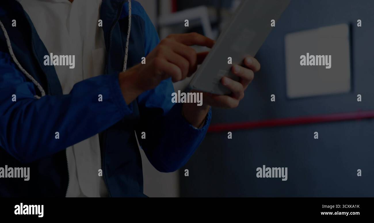 Holding tablet, technician wearing blue jacket tapping touchscreen in workshop, red stripe sign Stock Photo