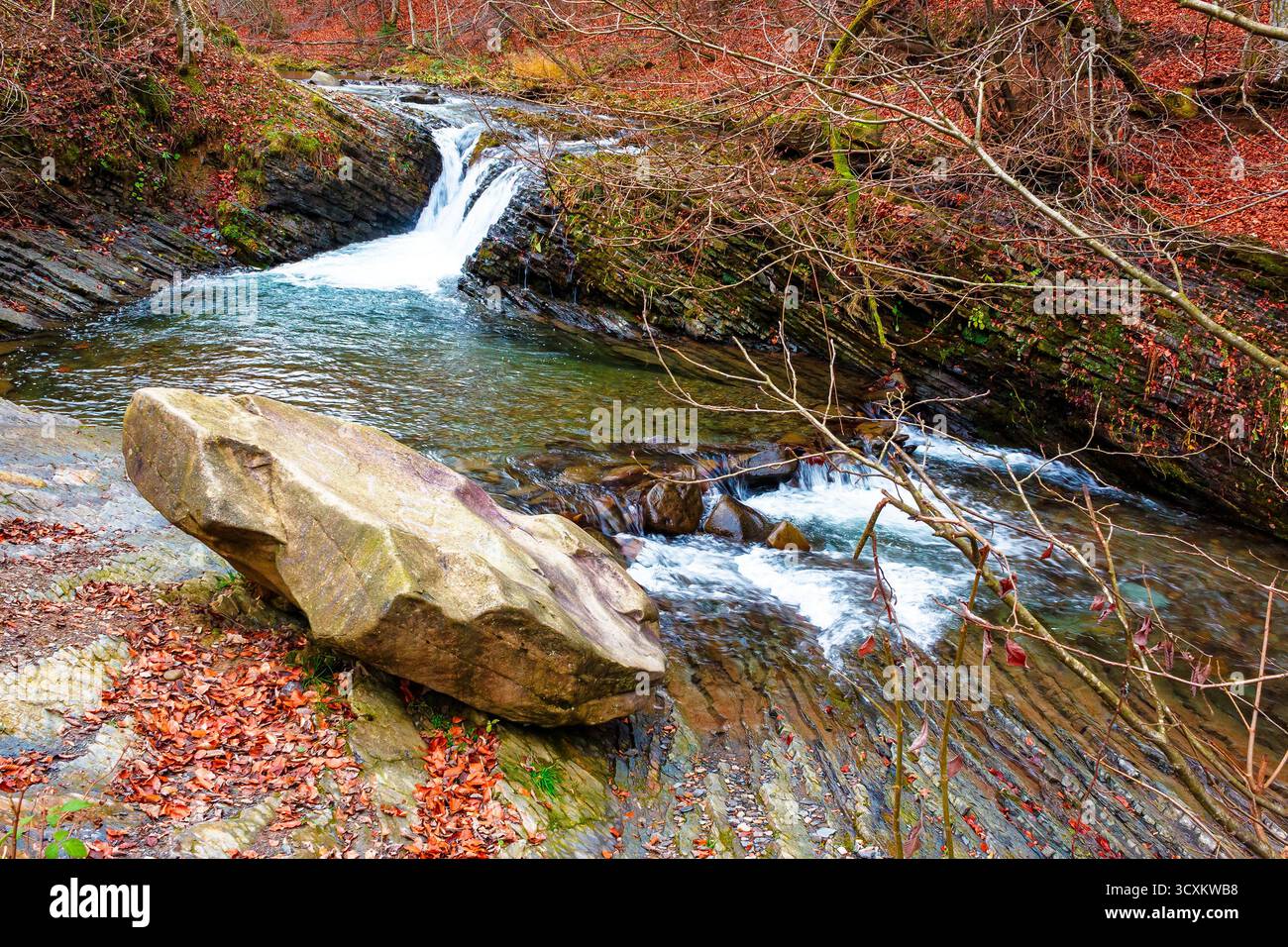 small waterfall on the turichka river in the forest near lumshory village of transcarpathia, ukraine. boulder on the shore. beautiful autumnal scenery Stock Photo
