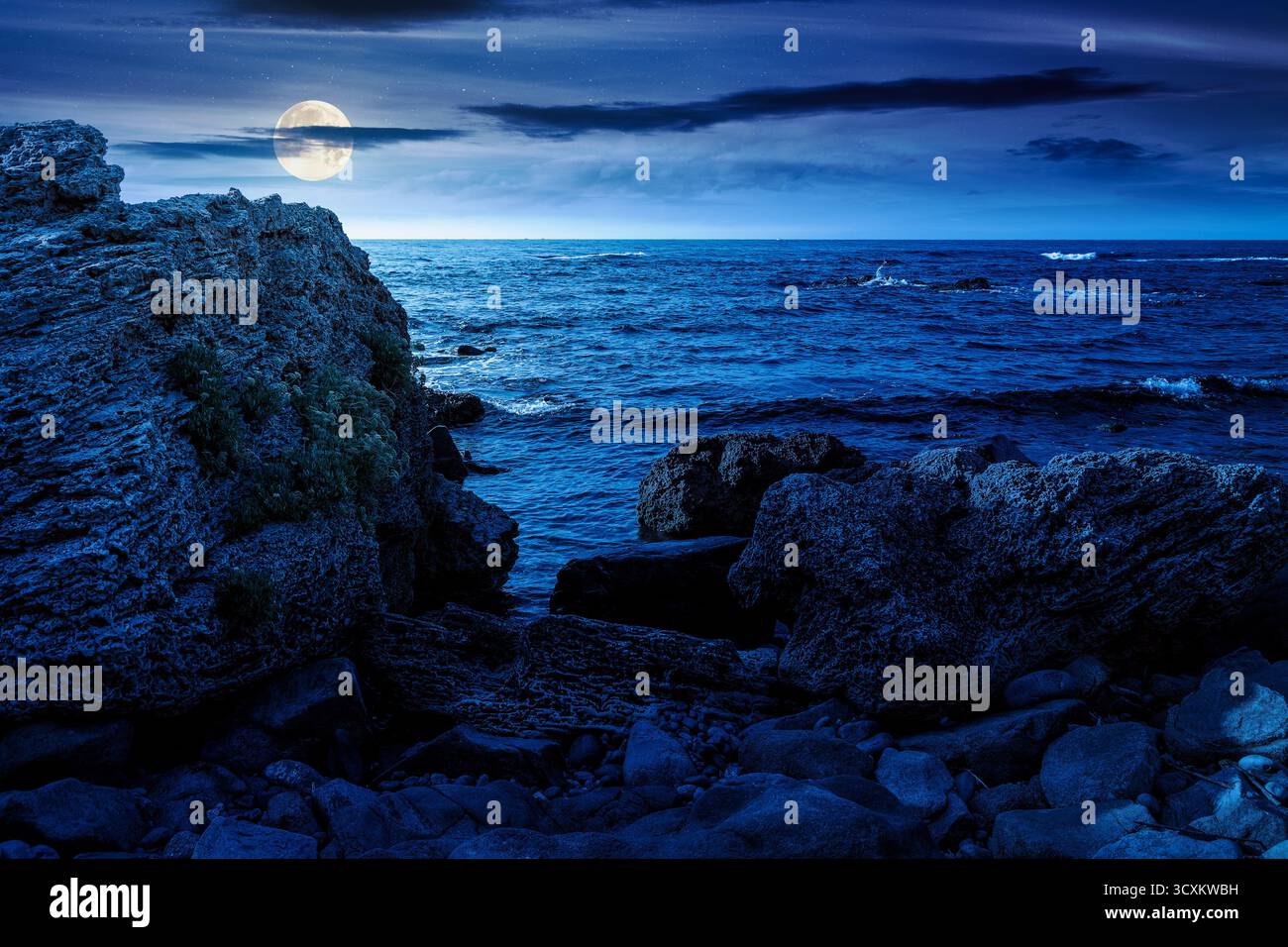 weekend on a rocky beach at the black sea under open dark sky at night. beautiful coastline in summer. seascape scenery with clouds above horizon in f Stock Photo