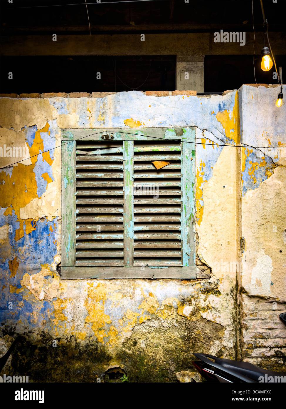 Old weathered wall with peeling paint and a rustic wooden shuttered window, illuminated by hanging bulbs Ipoh malaysia - shutters - Smartphone Captured Stock Image