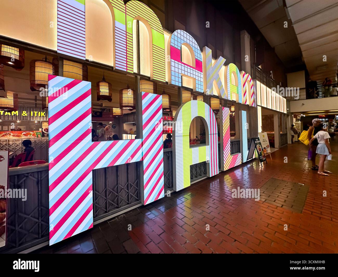 Illuminated signage of the vibrant Makan Hall at Pasar Besar Central Market food hall with colorful letters visitors at night kuala lumpur, malaysia - Smartphone Captured Stock Image