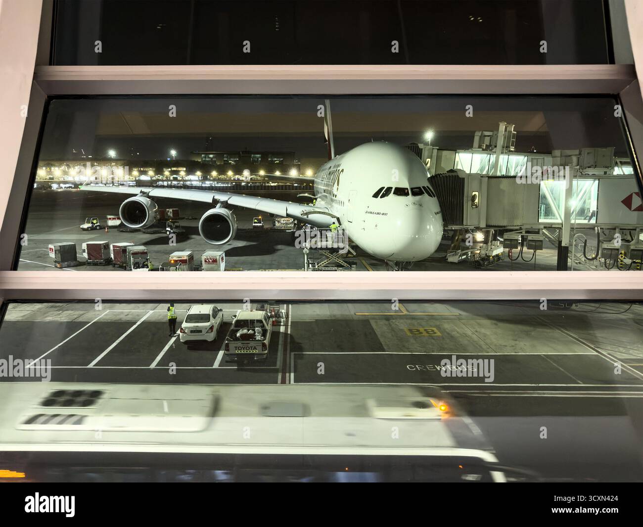 Airbus A380 Airplane at night parked at the terminal gate of a busy airport with city lights visible through large windows - Smartphone Captured Stock Image