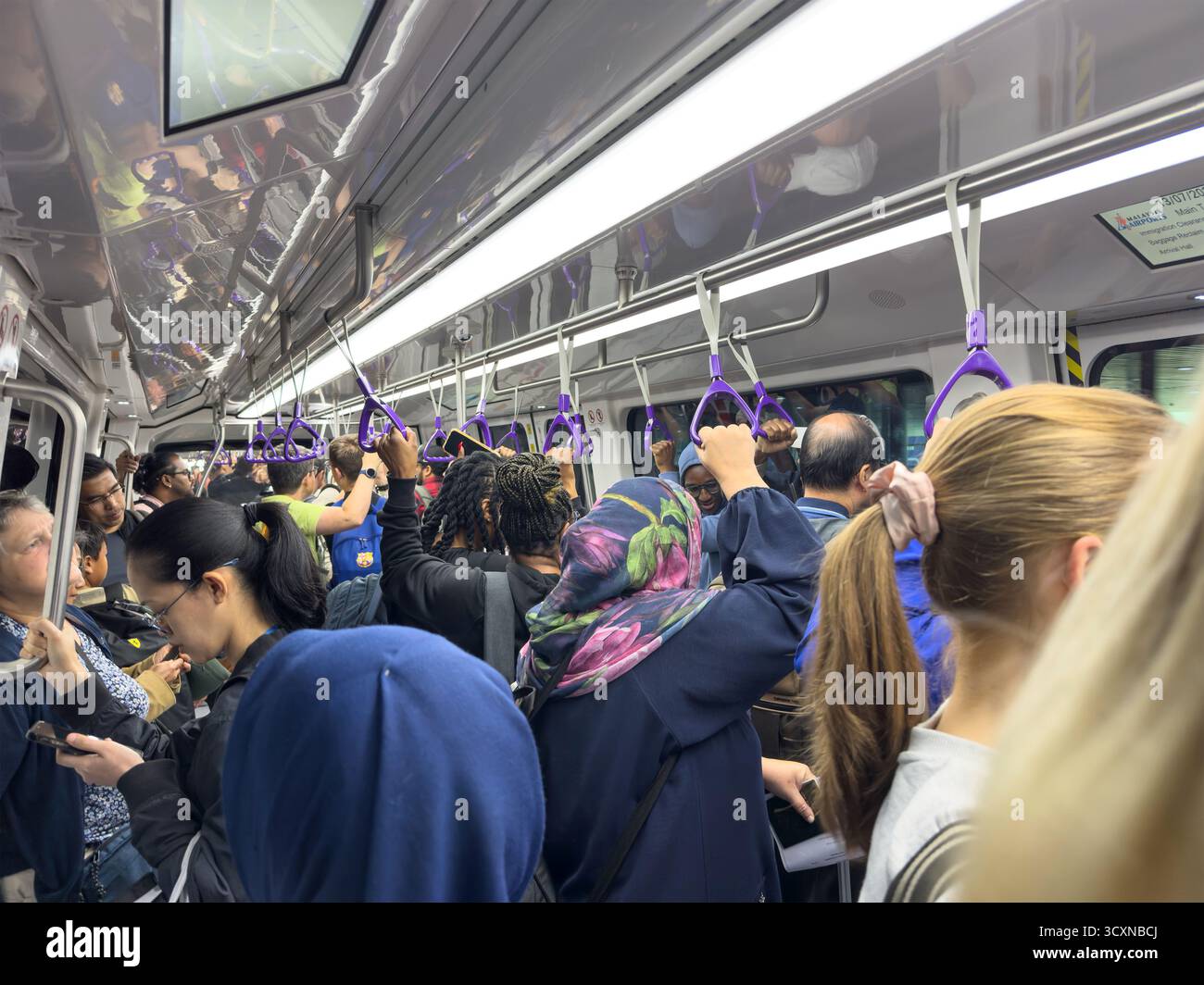 Crowded dubai airport shuttle train in motion with diverse passengers standing and holding onto purple handrails DXB rapid transit - Smartphone Captured Stock Image