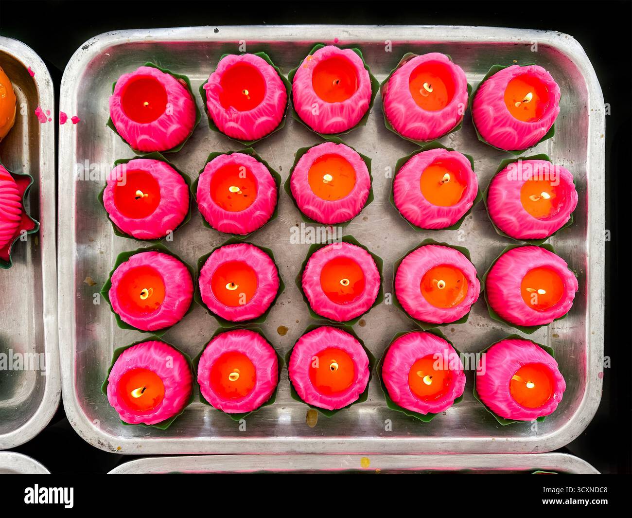 flat lay tray vibrant pink and orange lotus-shaped candles lit and arranged in a grid pattern viewed from above chinese temple kuala lumpur malaysia - Smartphone Captured Stock Image