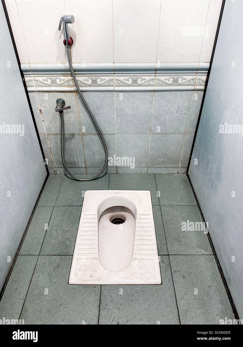 A clean and simple traditional squat toilet with a handheld bidet tap in a tiled restroom in kuala lumpur malaysia used by muslims - Smartphone Captured Stock Image