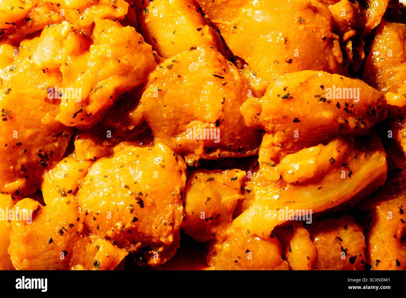 close-up of marinated chicken pieces seasoned for Spanish pinchos morunos, coated in a bright orange mix of spices and herbs under warm light Stock Photo