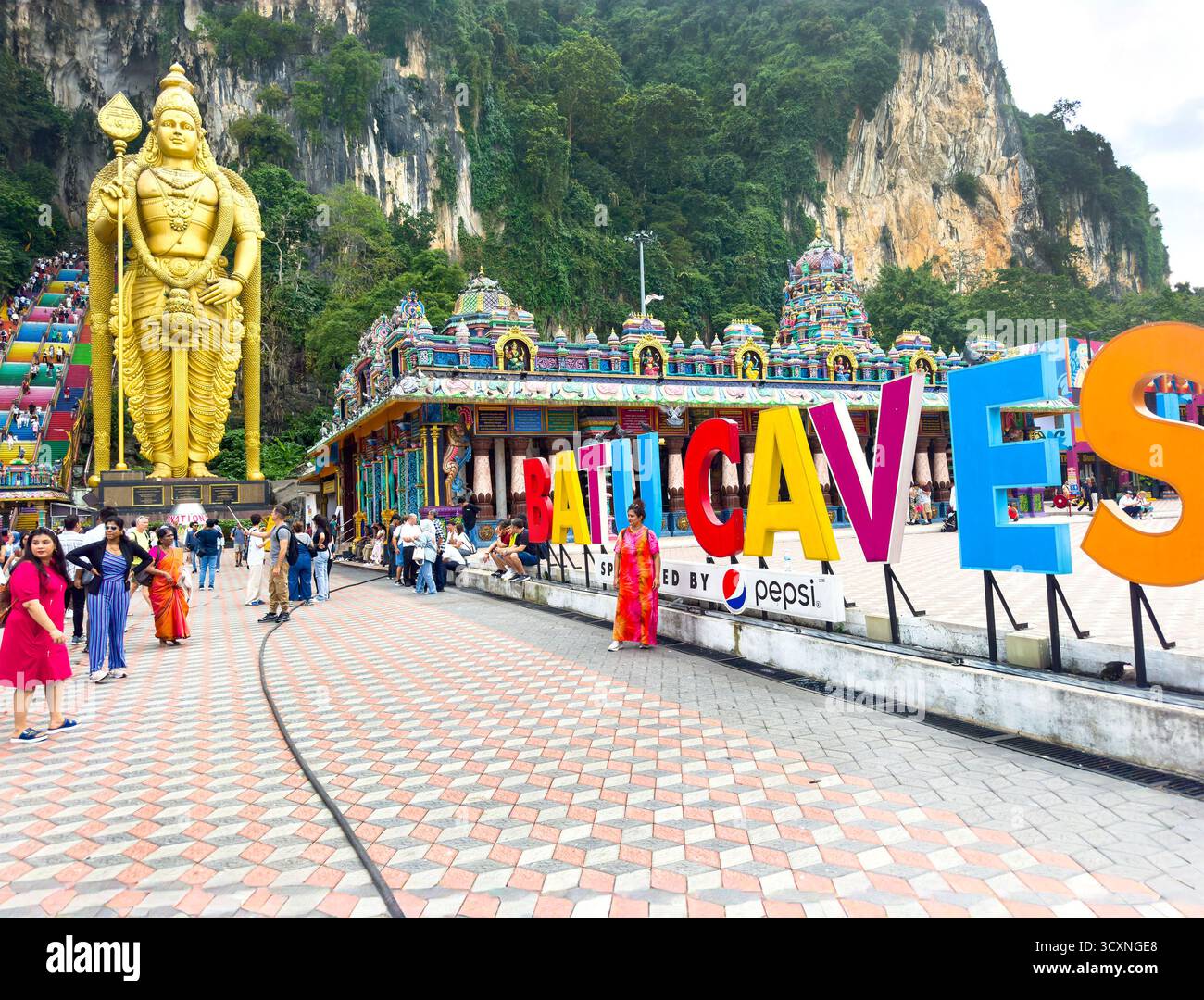 The entrance sign to Batu Caves featuring the giant golden Lord Murugan statue and colourful temple stairs against a rocky hill kuala lumpur malaysia - Smartphone Captured Stock Image