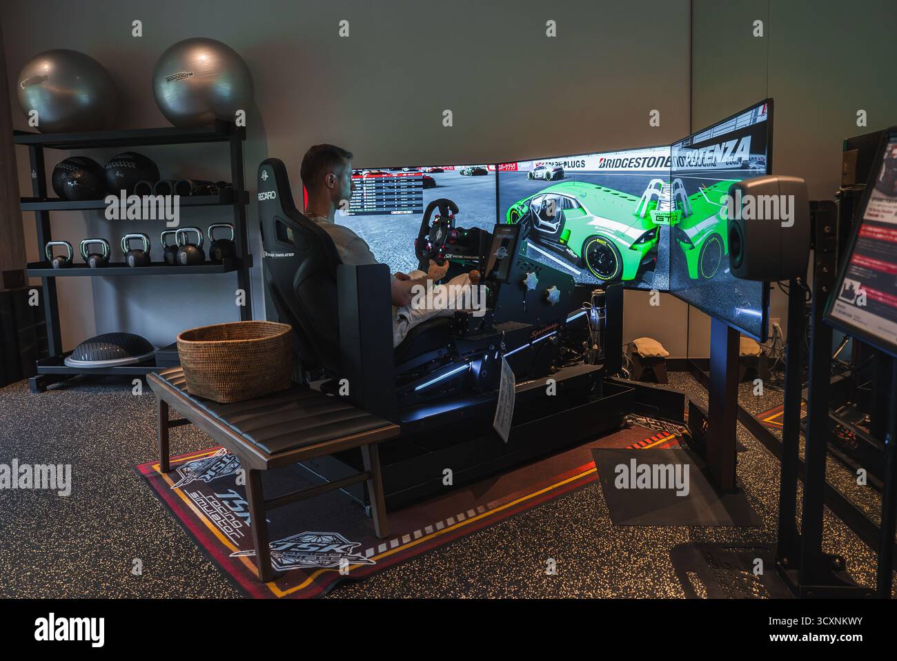 Man in racing simulator rig in hotel fitness room with GT car scene ...