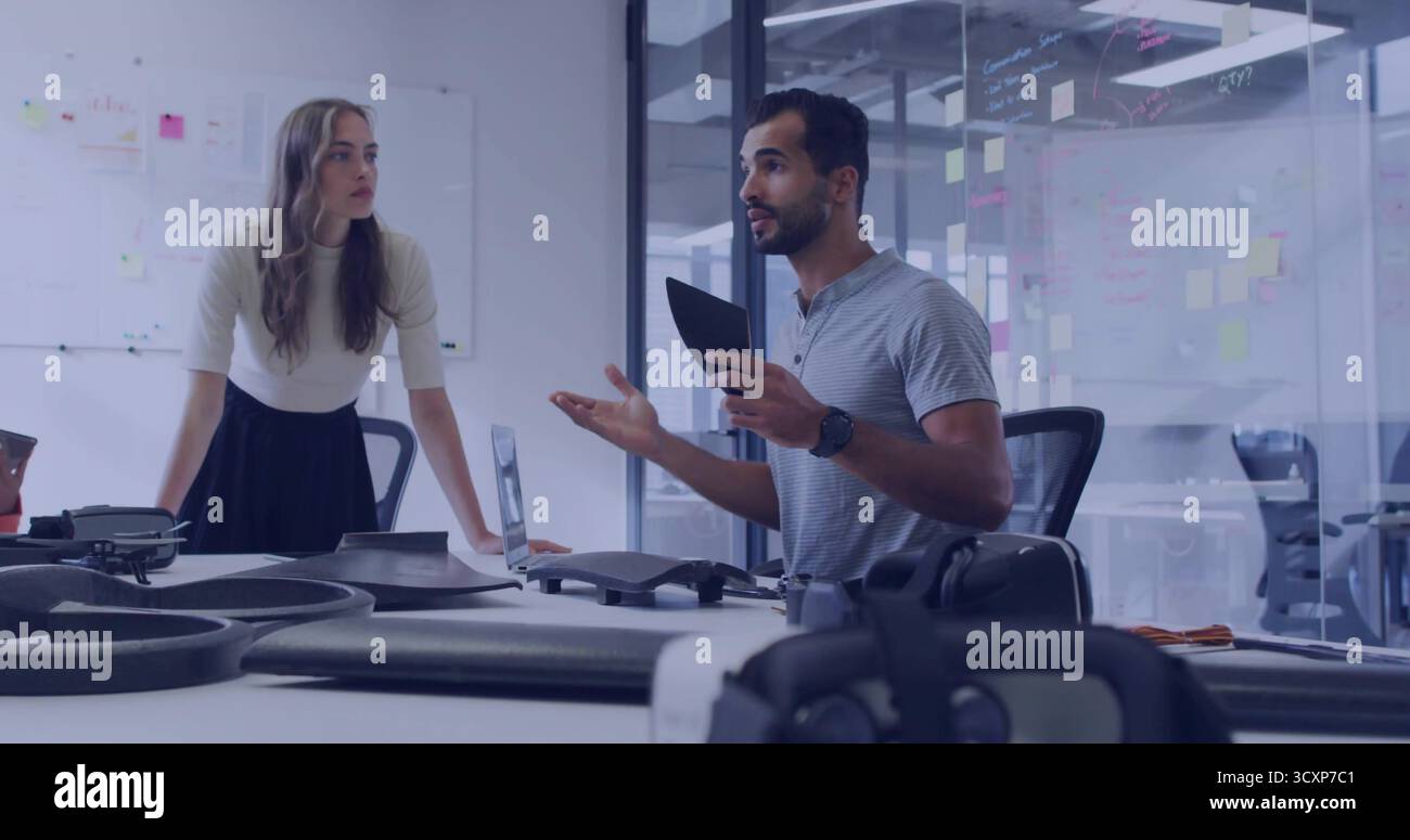Presenting engineer holding tablet gesturing at drone prototypes in office with whiteboard sketches Stock Photo