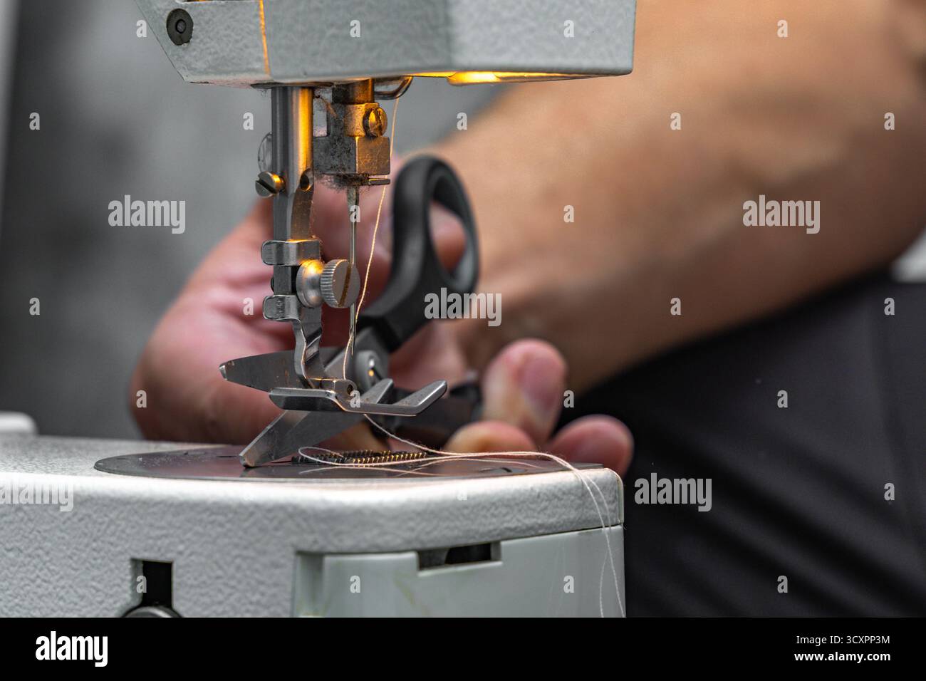 Close-up of hands sewing lightweight fabric on a sewing machine at home. Concept of handicraft, crafts, and small-scale textile production. Stock Photo