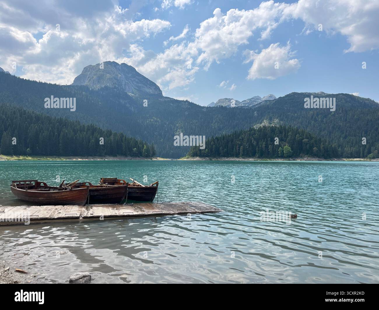 Wooden boats on a turquoise mountain lake surrounded by pine forests under a cloudy blue sky. - Smartphone Captured Stock Image