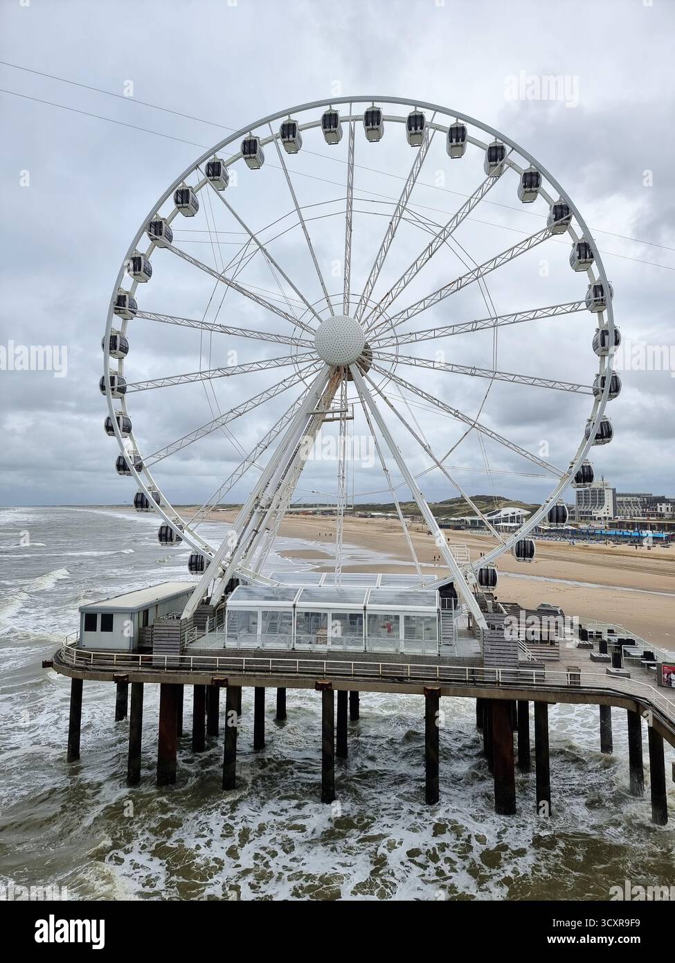 The Pier Skyview: ferris wheel in the North Sea on the pier in Scheveningen, The Netherlands with dark clouds in autumn weather; beach in background - Smartphone Captured Stock Image