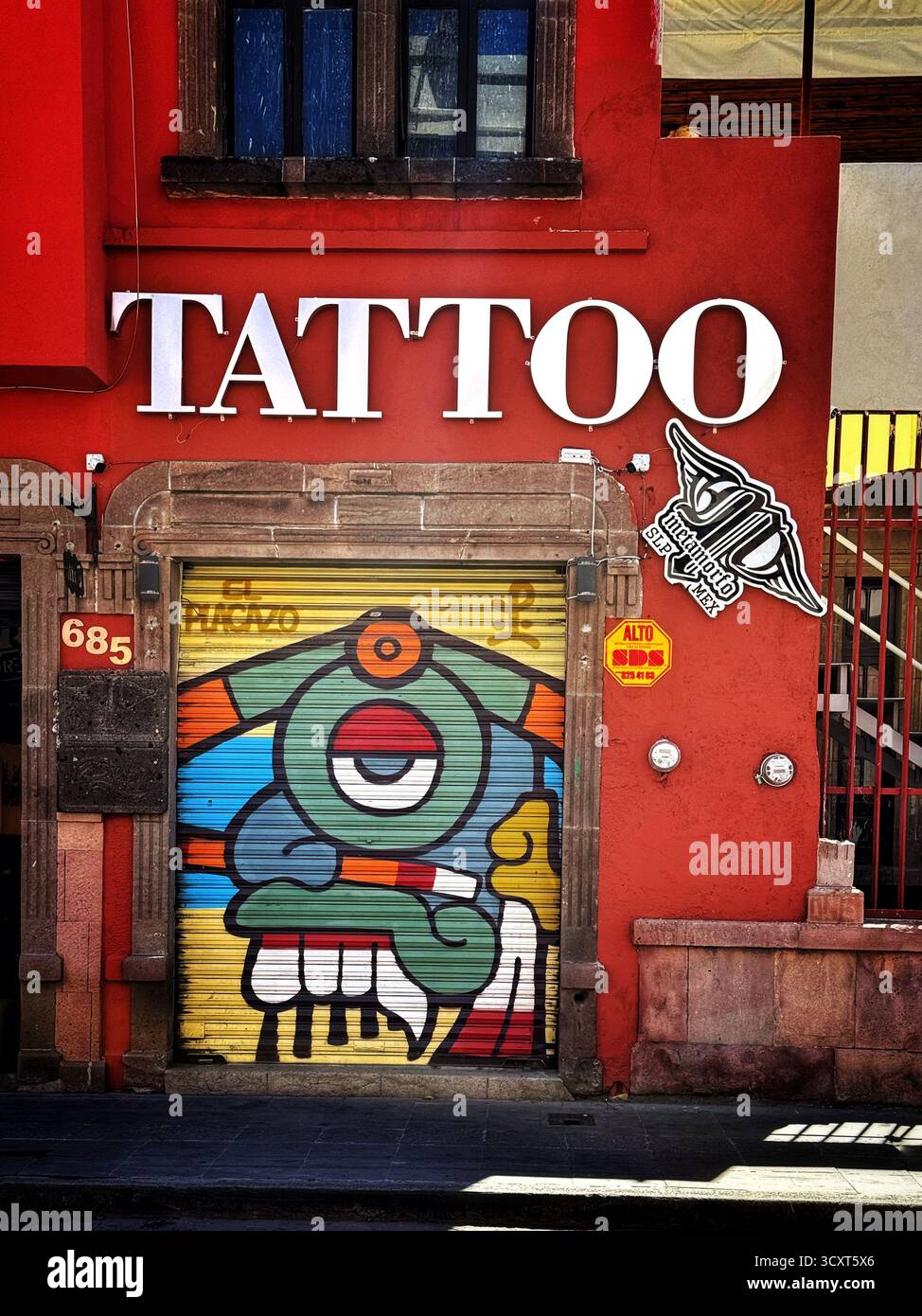 Vibrant tattoo parlor entrance with street art mural featuring a colorful abstract design in an urban setting - Smartphone Captured Stock Image