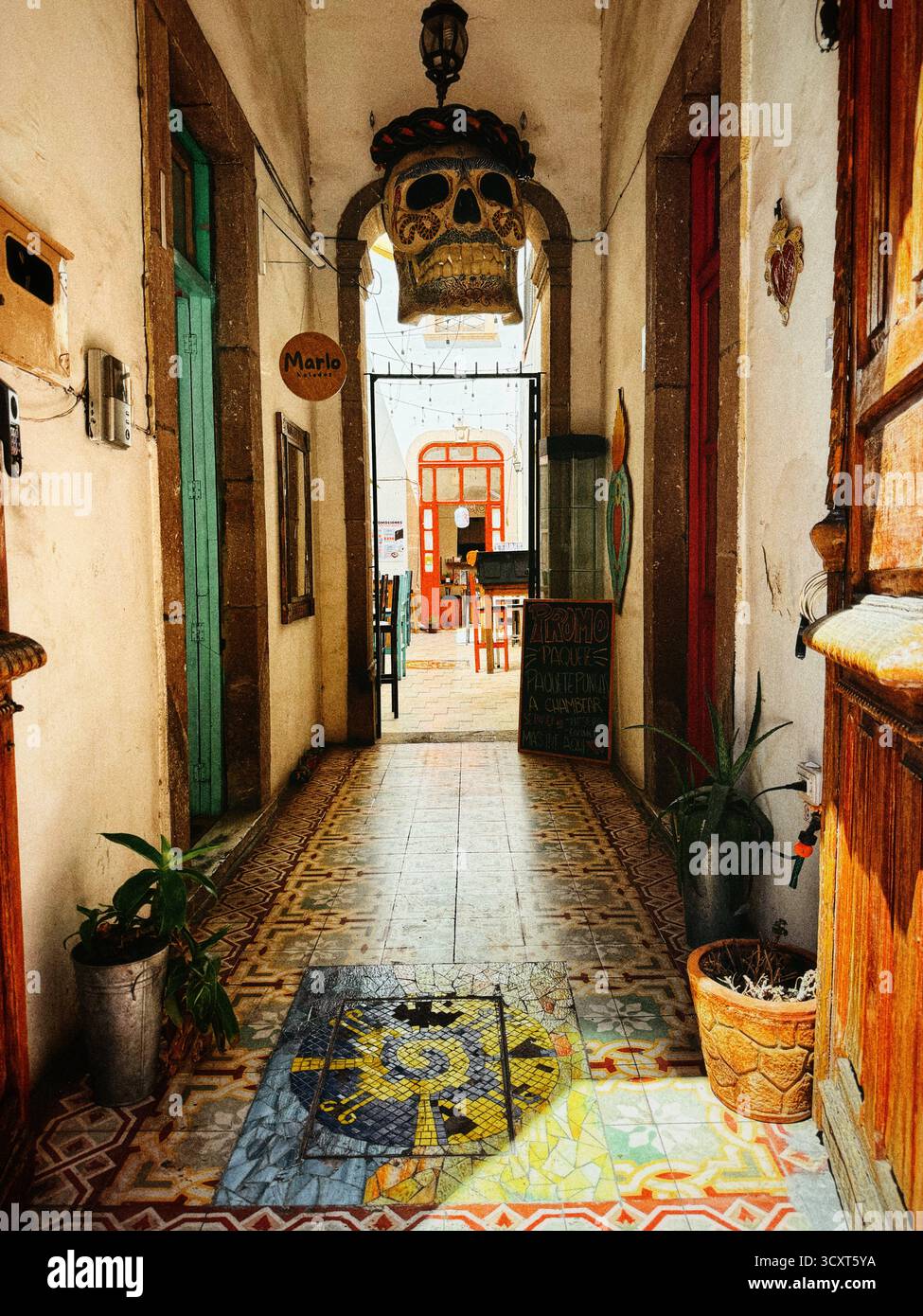 Vibrant entrance hallway with decorative tiles and colorful doors leading to an outdoor seating area with a traditional skull decoration - Smartphone Captured Stock Image