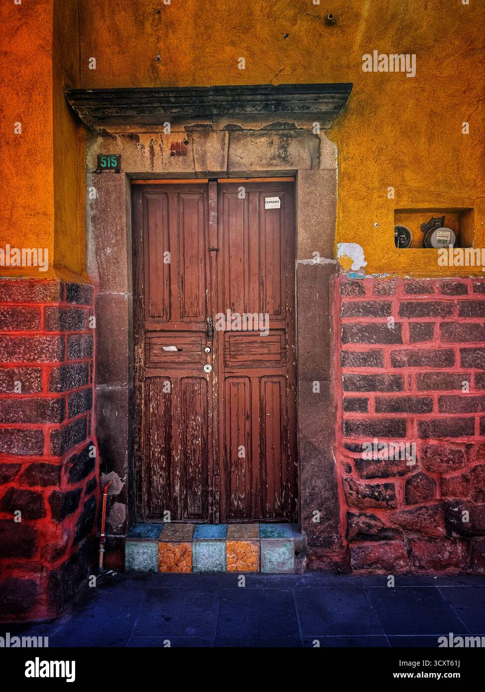 Colorful rustic wooden door set in a vibrant yellow and red textured wall with ceramic decorations in urban street setting - Smartphone Captured Stock Image
