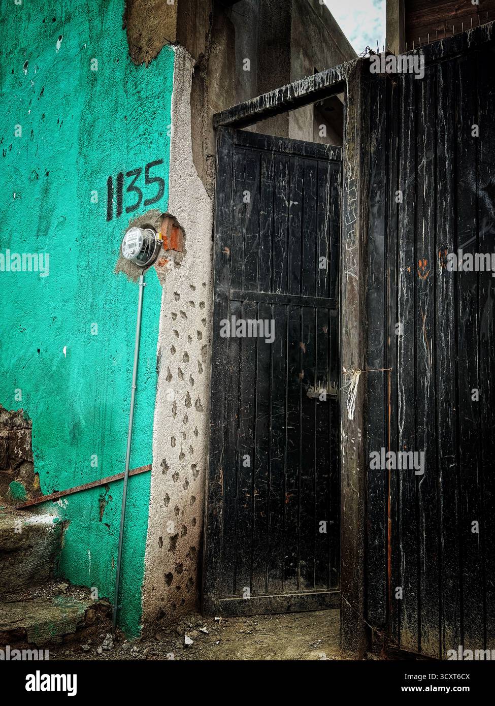 Urban scene with a weathered turquoise wall, a black gate and the number 1135 painted on a concrete surface - Smartphone Captured Stock Image