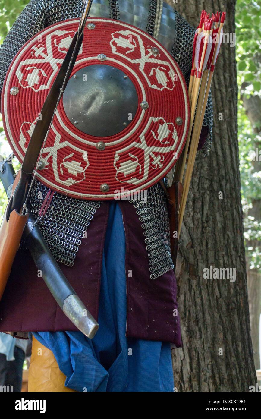 A medieval knight in full armor with shield and swords standing near a ...