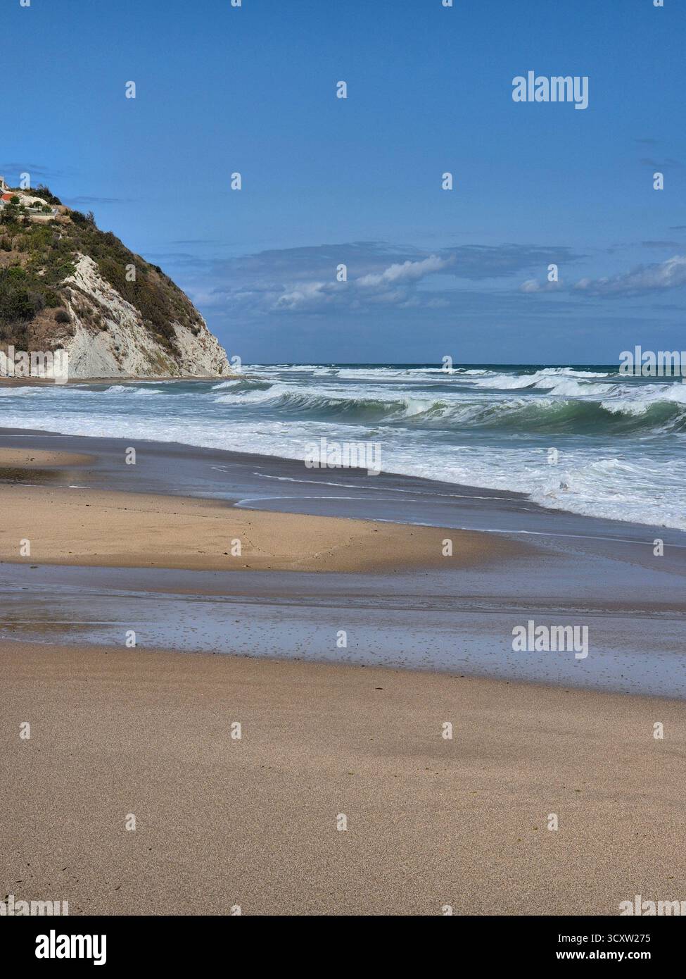 Seascape with a wavy sea rolling onto a sandy shore. In the background on the left, a white or light-colored rock rises above the water. The sky is br - Smartphone Captured Stock Image