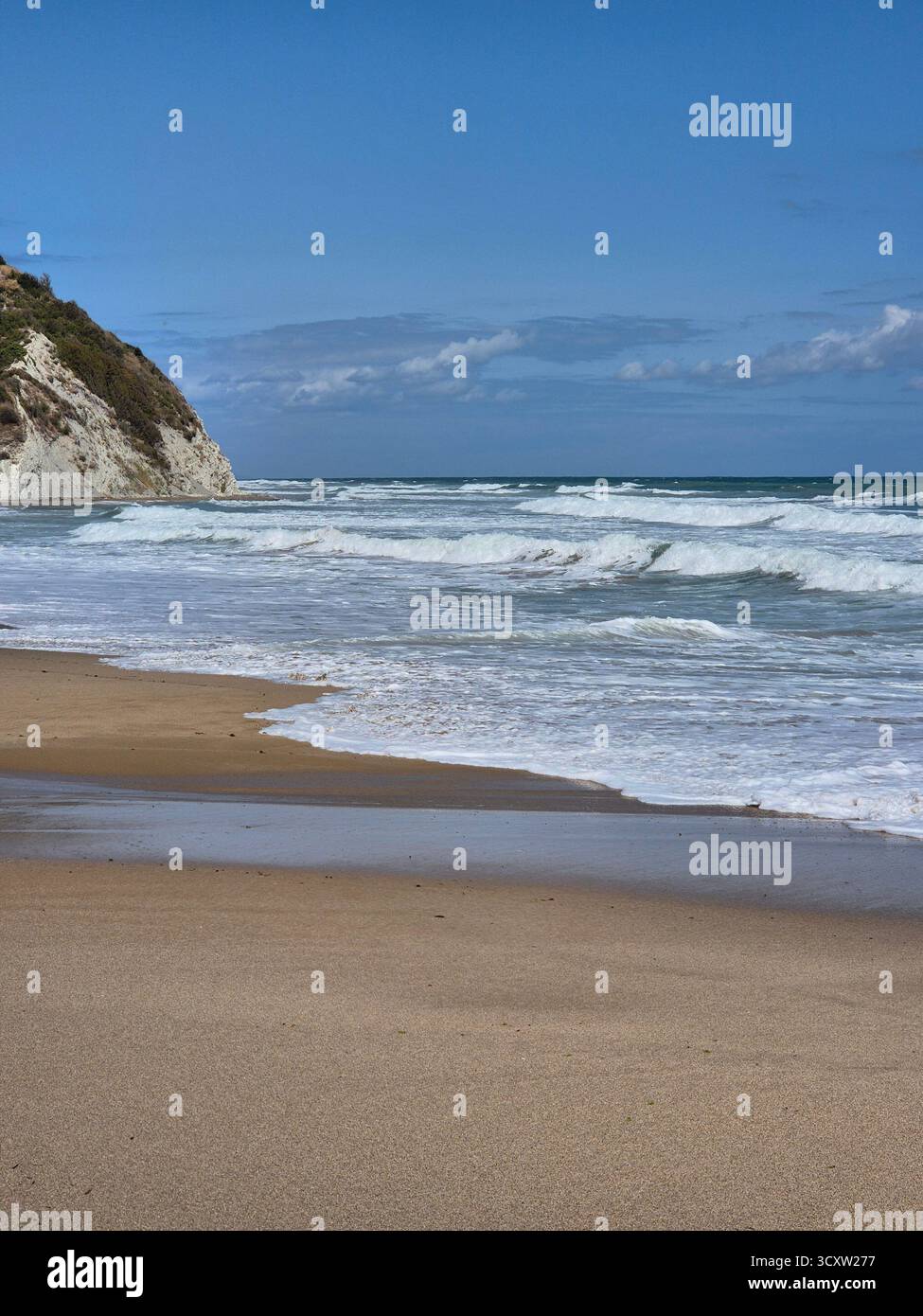 Seascape with a wavy sea rolling onto a sandy shore. In the background on the left, a white or light-colored rock rises above the water. The sky is br - Smartphone Captured Stock Image