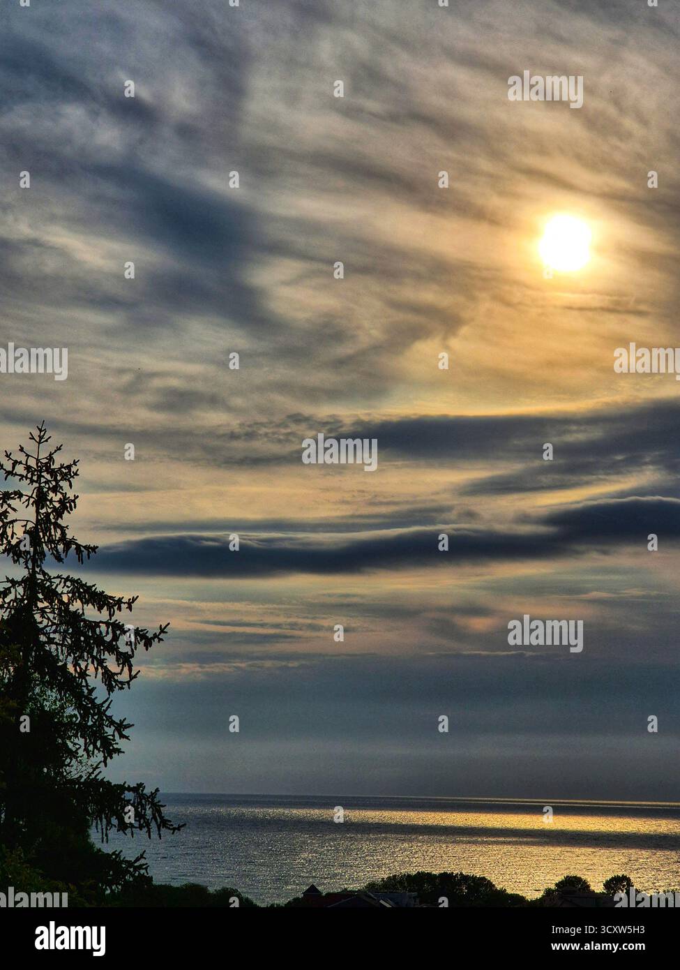 Seascape at sunset or dawn. The sky is covered with long horizontal clouds in shades of blue, gray and light yellow. The sun shines a bright disk thro - Smartphone Captured Stock Image