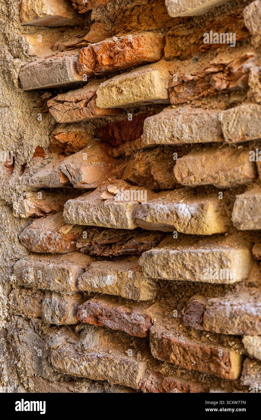 An ancient brick wall with a few bricks eroded and missing. The wall is brown and has a rough texture. The missing bricks create a sense of emptiness Stock Photo