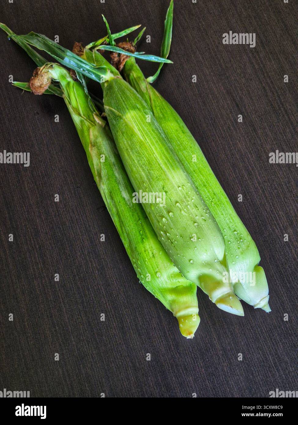 Three fresh corn cobs in their green husks on wooden background. corn on the cob - Smartphone Captured Stock Image