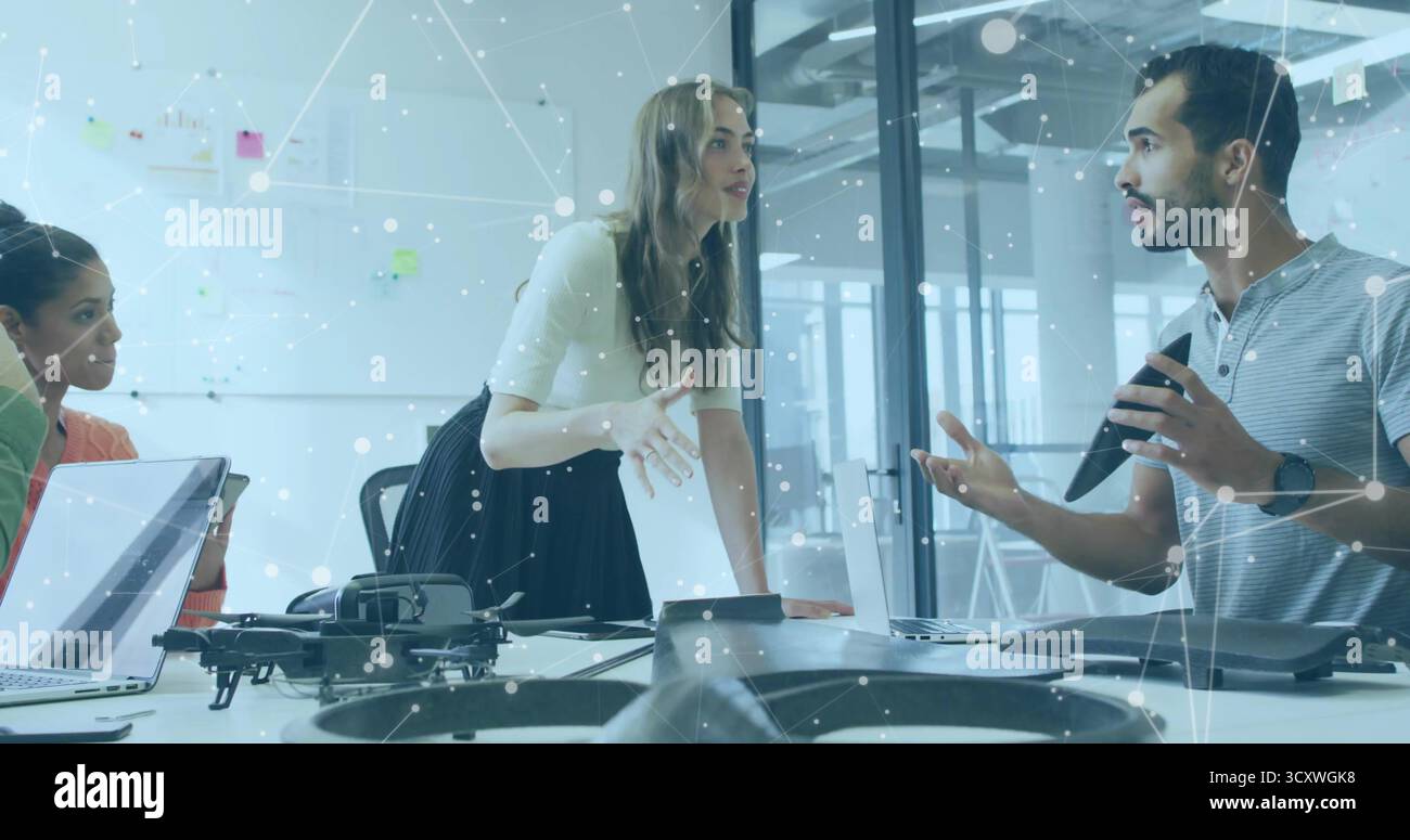 Discussing drone project, three colleagues leaning around conference room table with quadcopter Stock Photo