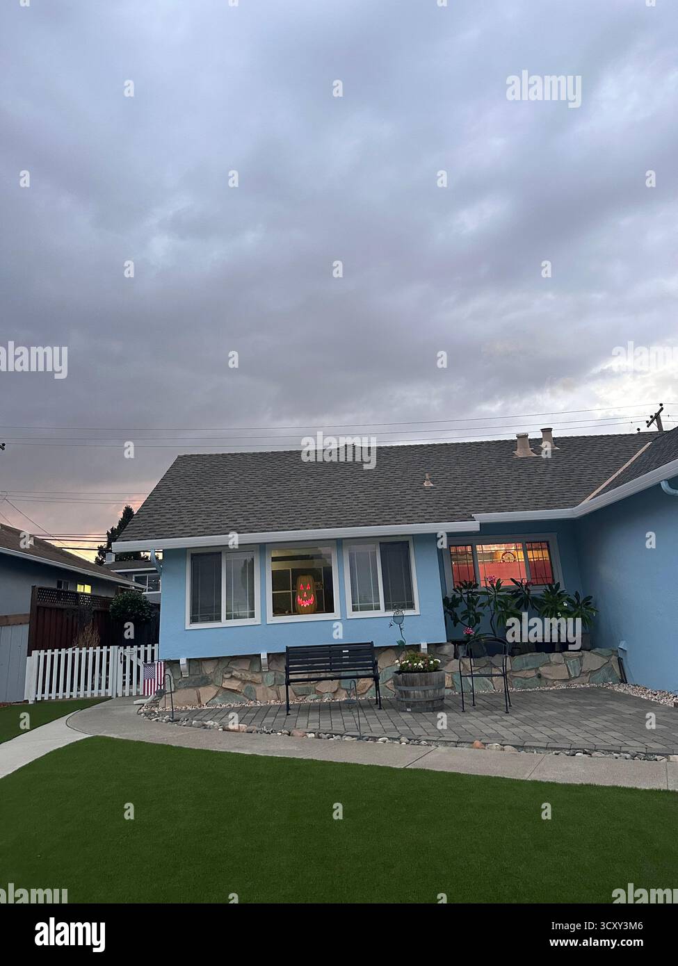 Glowing Pumpkin Face in Suburban Window – California Halloween Scene - Smartphone Captured Stock Image