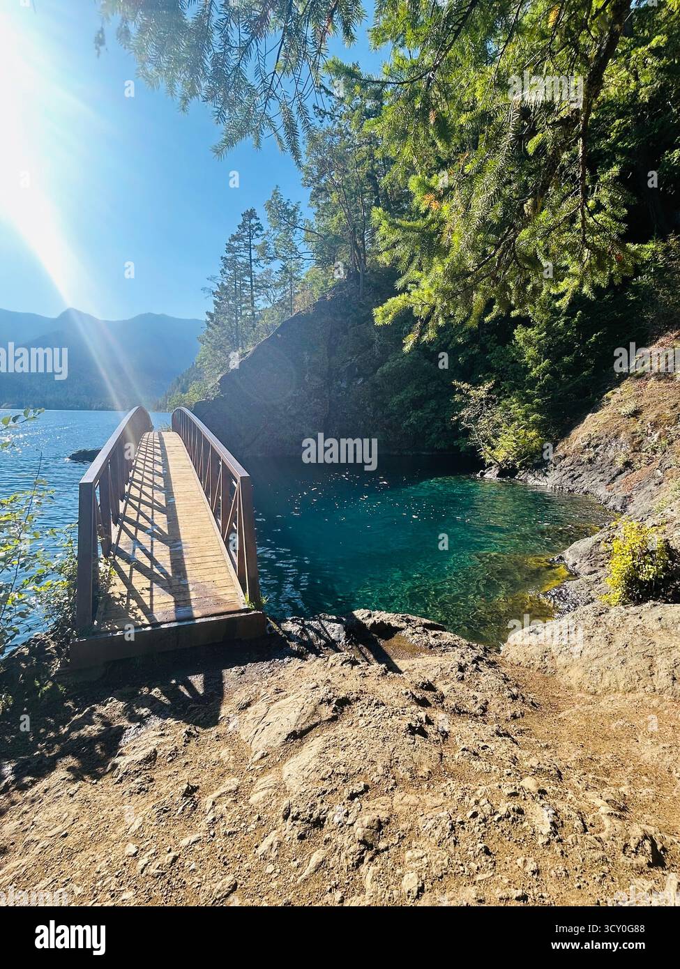 The iconic bridge spans Devils Punch Bowl in Olympic National Park, Washington, on a bright sunny day. The crystal blue water below contrasts with the - Smartphone Captured Stock Image