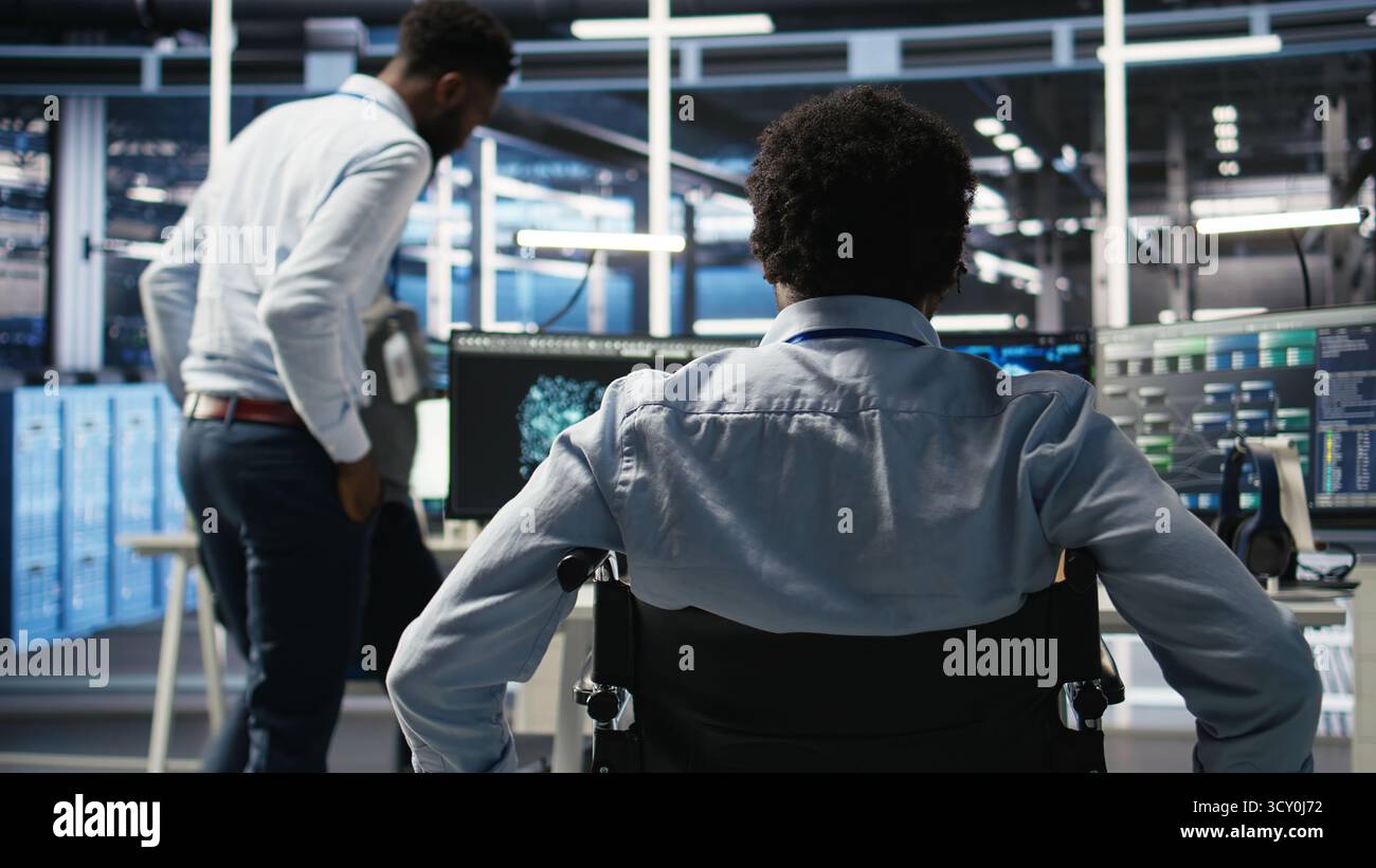 Data center programmer in wheelchair entering office uses AI node tree program to minimize system downtime. Server room IT expert in disability uses machine learning visual programming tool, camera A Stock Photo